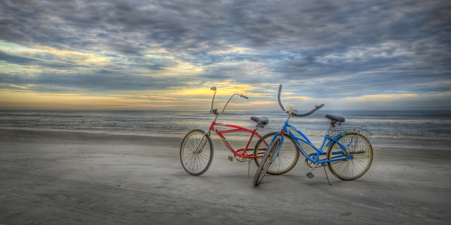 A black and white color image of his and hers Schwinn beach cruisers at sunrise on the beach