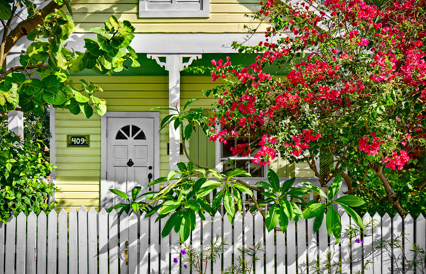 A photo of a key lime colored cottage home surrounded by tropical flowering plants in Key West, Florida