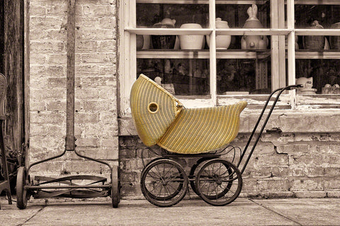 A photo of an old antique push lawnmower and Baby Carriage outside an antique shop