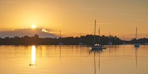 A photo of the sun rising with sailboats on the Indian River